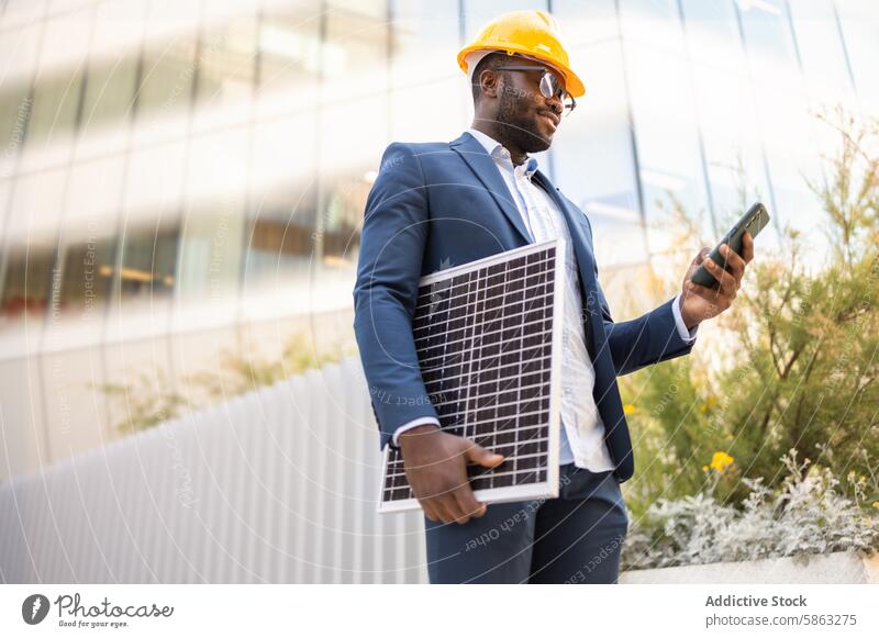 Schwarzer Geschäftsmann mit Sonnenkollektor und Smartphone Business Mann Afroamerikaner Anzug Schutzhelm im Freien Technik & Technologie Energie nachhaltig