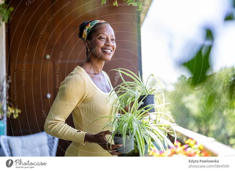 Lächelnde Frau mit Topfpflanzen auf dem Balkon zu Hause Menschen Freude schwarz natürlich attraktiv schwarze Frau Fröhlichkeit Glück echte Menschen reif