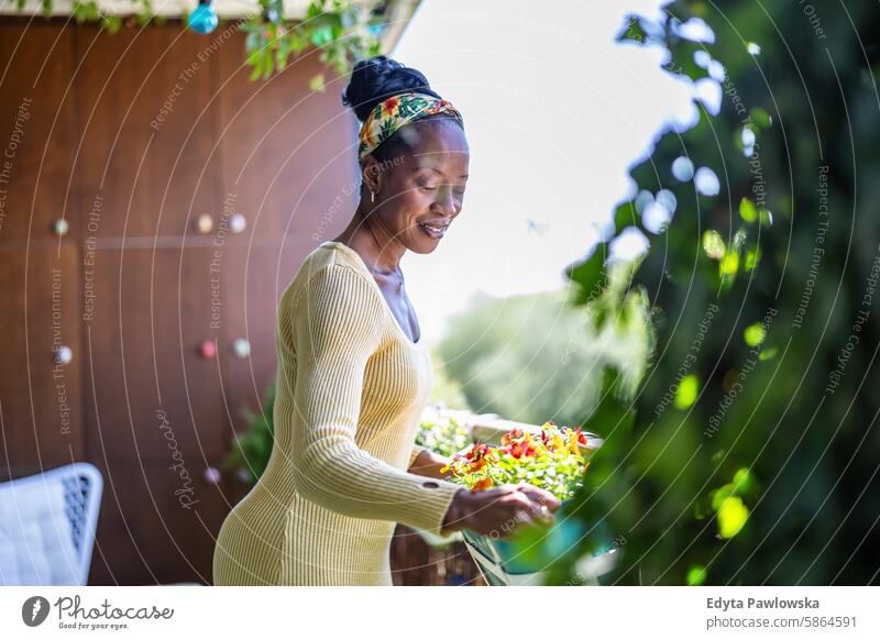 Schöne Frau bewässert Pflanzen auf dem Balkon Menschen Freude schwarz natürlich attraktiv schwarze Frau Fröhlichkeit Glück echte Menschen reif Erwachsener