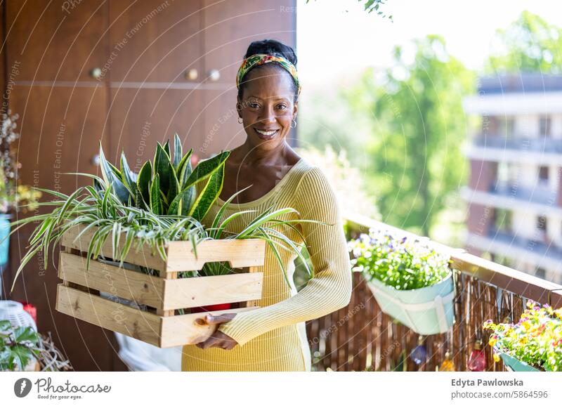 Lächelnde Frau mit Topfpflanzen auf dem Balkon zu Hause Menschen Freude schwarz natürlich attraktiv schwarze Frau Fröhlichkeit Glück echte Menschen reif