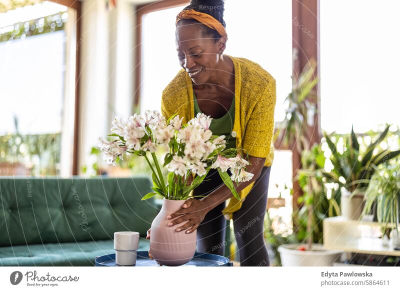 Porträt einer lächelnden Frau, die zu Hause eine Vase mit Blumen hält Menschen Freude schwarz natürlich attraktiv schwarze Frau Fröhlichkeit Glück