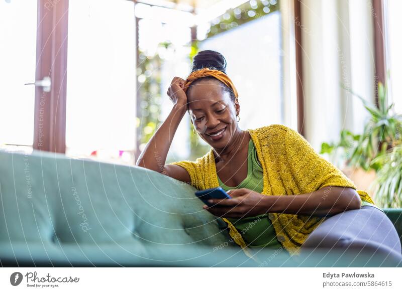 Frau benutzt Smartphone, während sie sich zu Hause auf dem Sofa entspannt Menschen Freude schwarz natürlich attraktiv schwarze Frau Fröhlichkeit Glück
