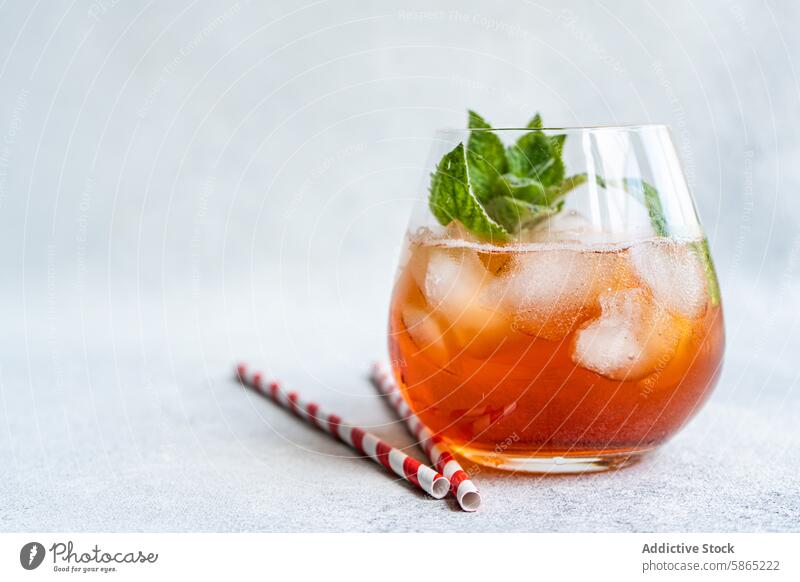 Erfrischender Cola-Cocktail mit Minze und Eis im Glas Getränk Koks Stroh Papier rot gestreift gekühlt Garnierung Blätter Würfel grau Hintergrund Textur