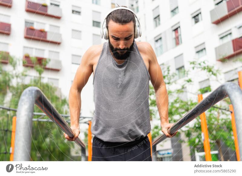 Mann beim Sport im Freien in Poblenou mit Kopfhörern Übung poblenou Barcelona ärmelloses Hemd Dip Parallelbarren urban Gebäude Fokus Fitness Lifestyle