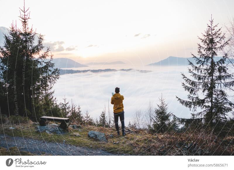 Ein Abenteurer fotografiert mit seinem Mobiltelefon den Sonnenuntergang und die Wolken darunter. Erinnerungen mit Technologie festhalten. Beskiden, Tschechische Republik