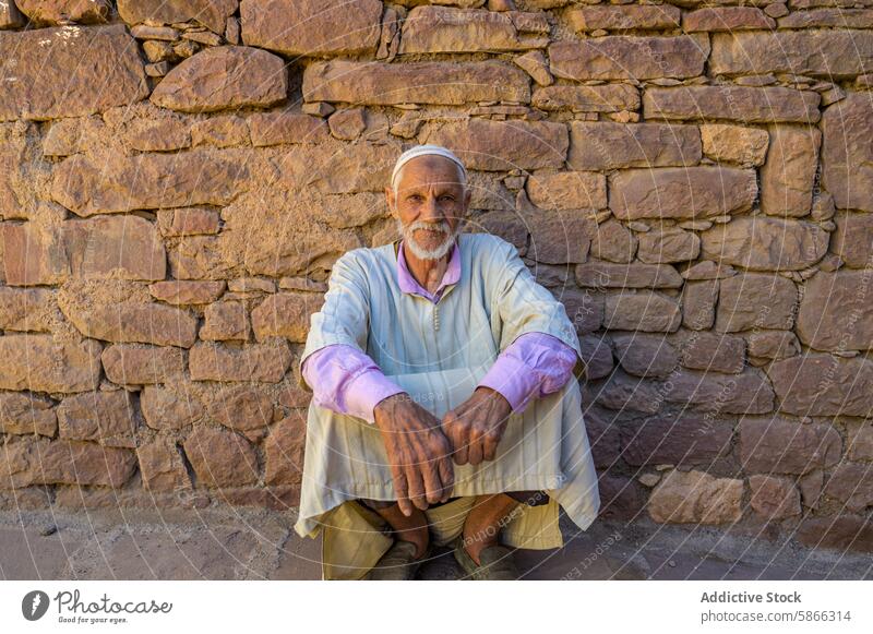 Älterer marokkanischer Mann in traditioneller Kleidung an einer Steinmauer sitzend Holunderbusch Marokkaner Wand kulturell Erbe Historie Marokko Nordafrika