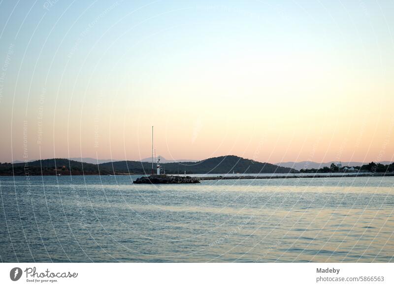 Romantische Abendstimmung am Meer mit dem Licht der Abendsonne mit Leuchtturm und Pier am Hafen in der Bucht von Ayvalik am Ägäischen Meer in der Provinz Balikesir in der Türkei