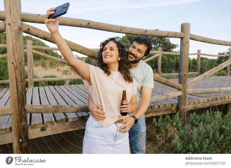 Ein Paar genießt ein Bier und macht ein Selfie in der Natur Smartphone im Freien Holzdeck lässig freudig friedlich Mann Frau Sommer Freizeit Erholung trinken