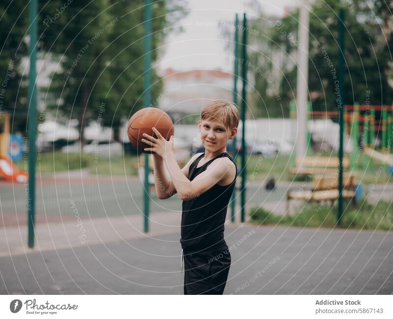 Junger Teenager lächelt beim Basketballspielen im Freien Spielen Gericht Sport Stadtpark Spielplatz Gesundheit Aktivität Fitness Ball Sportbekleidung Freizeit