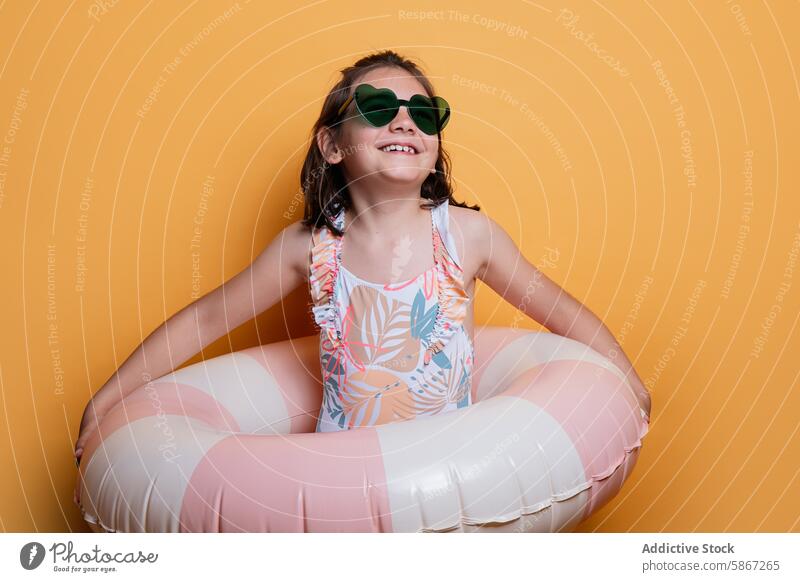 Mädchen mit Sommerbadeanzug und Sonnenbrille im Studio Badebekleidung aufblasbar Ring orange Hintergrund Atelier Lächeln jung Kind geblümt herzförmig Glück