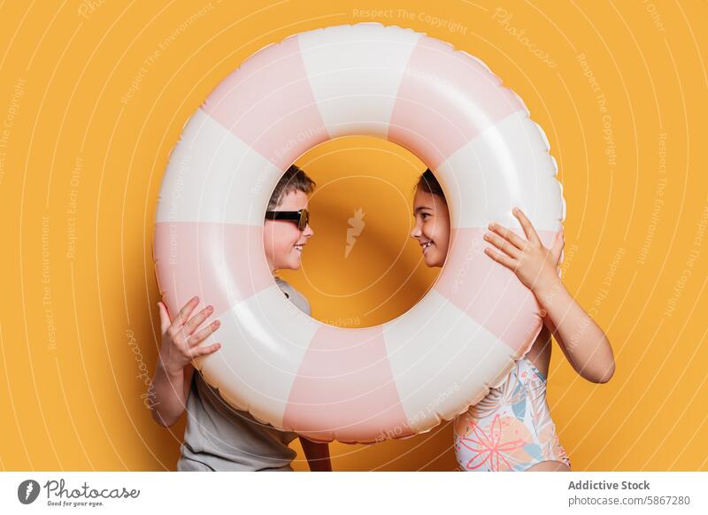 Zwei Kinder spielen mit einem Schwimmring in einer sommerlichen Szenerie Sommer Spaß Freude gelber Hintergrund Atelier Junge Mädchen spielerisch Fröhlichkeit