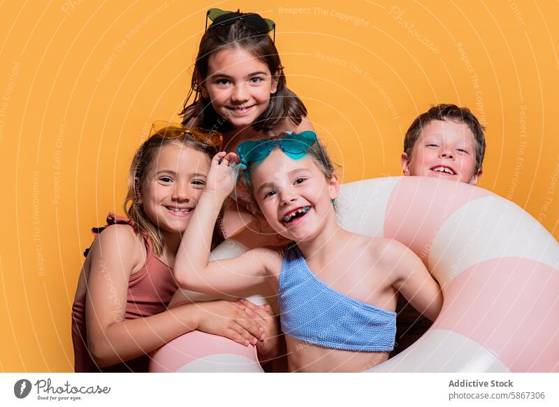 Fröhliche Kinder mit Sommerrequisiten in einem Studio Atelier aufblasbar Ring freudig Pose Hintergrund gelb heiter Mädchen Junge Badebekleidung Sonnenbrille