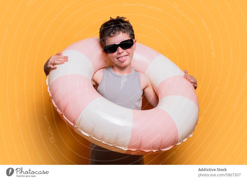 Junge mit Schwimmring in einem sommerlichen Studio-Shooting Sommer Atelier Sonnenbrille oranger Hintergrund spielerisch heiter Jugend Fröhlichkeit Spaß Freizeit