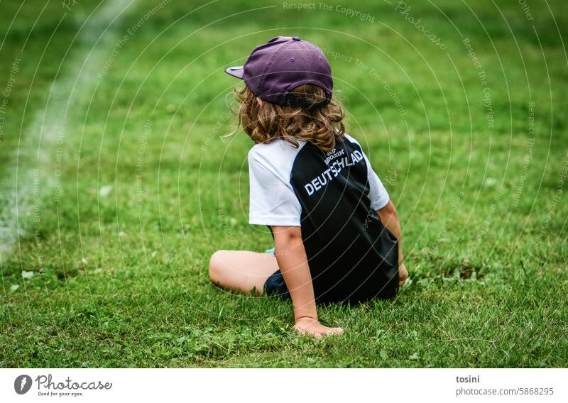 Ein Junge im Fußballtrikot macht Pause auf dem Spielfeld Wiese Rasen Kind Fußballplatz Europameisterschaft EM2024 Mütze grün Sport Freizeit & Hobby Sportrasen