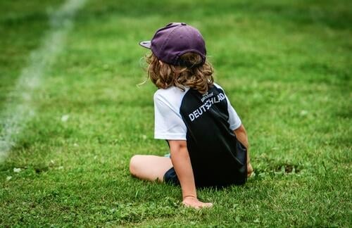 Ein Junge im Fußballtrikot macht Pause auf dem Spielfeld Wiese Rasen Kind Fußballplatz Europameisterschaft EM2024 Mütze grün Sport Freizeit & Hobby Sportrasen