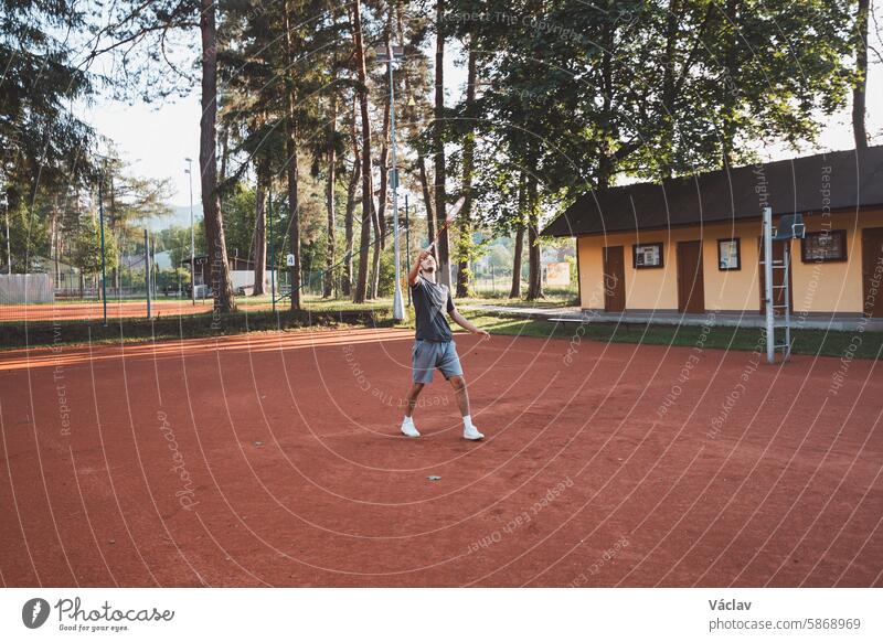 Schwarzhaariger Sportler mit einem Lächeln auf dem Gesicht spielt Badminton auf einem Sandplatz. Begeisterung für den Amateursport. Neue Bewegungsabläufe lernen