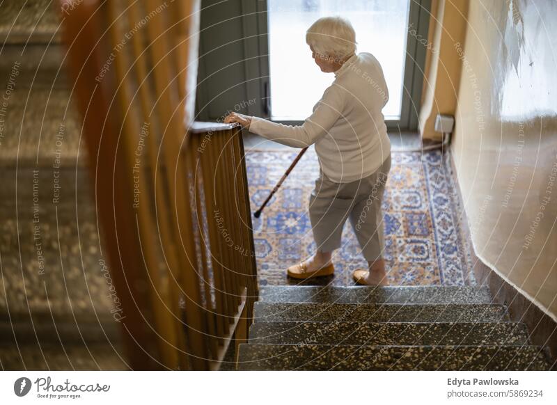 Ältere Frau geht die Treppe hinunter und stützt sich auf einen Holzstock Menschen Senior reif älter heimwärts Haus alt Alterung häusliches Leben Großmutter