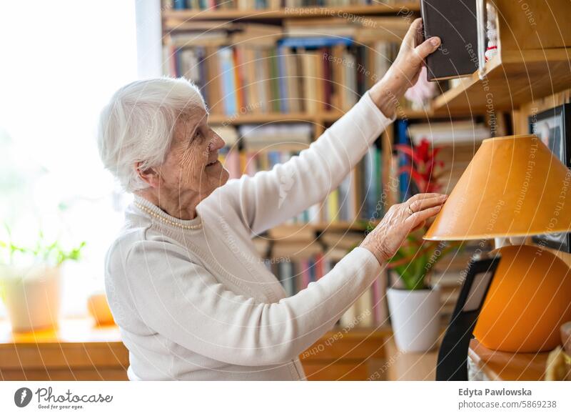 Ältere Frau wählt ein Buch aus dem Bücherregal zu Hause aus Lächeln Glück genießend positiv Freude zufrieden Menschen Senior reif älter heimwärts alt Alterung