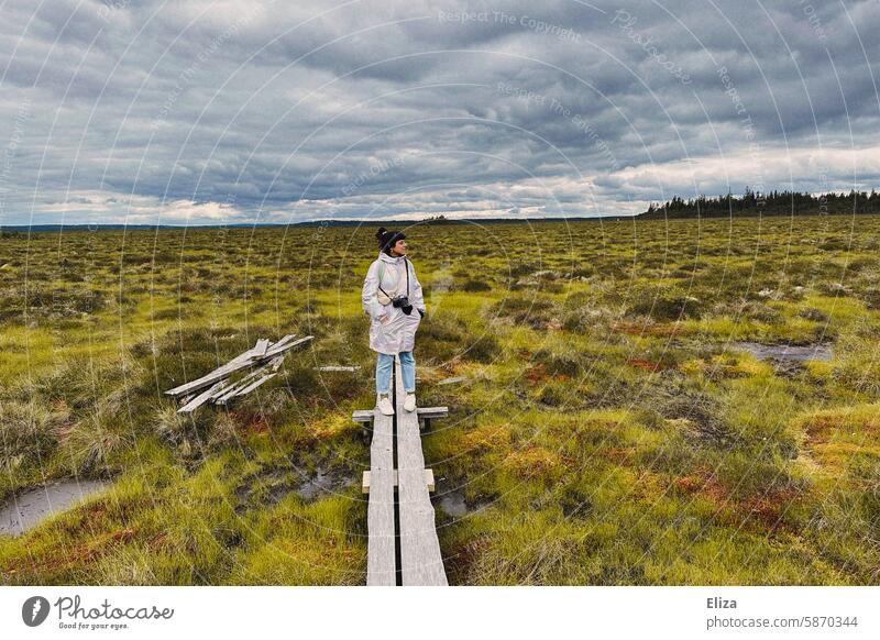 Frau mit Kamera steht auf einem Holzsteg in einem Moorgebiet Steg kamera bewölkter Himmel Wanderung Landschaft Natur Wege & Pfade Ausflug Naturschutzgebiet