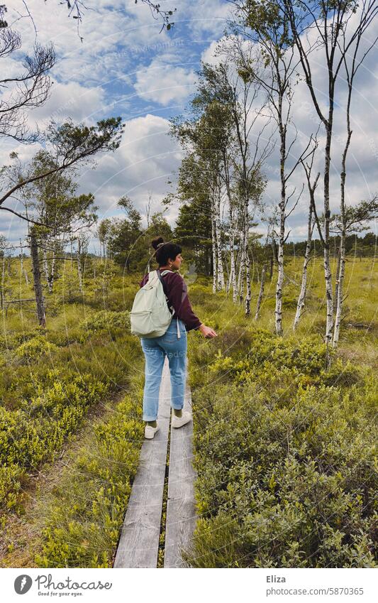 Eine Frau mit Rucksack läuft einen Steg durch die Natur entlang spaziergang Birken Wald Bäume Wanderung Moor Landschaft Naturschutzgebiet grün jeans Spaziergang