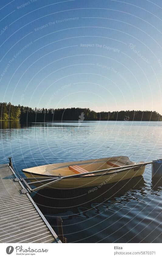 Kleines Ruderboot liegt an einem Steg eines Sees Ufer Natur blauer Himmel Sonnenschein Idylle Landschaft Wasser ruhig Seeufer Bäume Wald Paddel klein