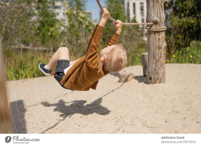 Junge schwingt an einem Seil in einem sonnigen Park pendeln Freude spielen im Freien Kind Sommer Aktivität Spaß Erholung Schaukelanlage Genuss Freizeit Natur