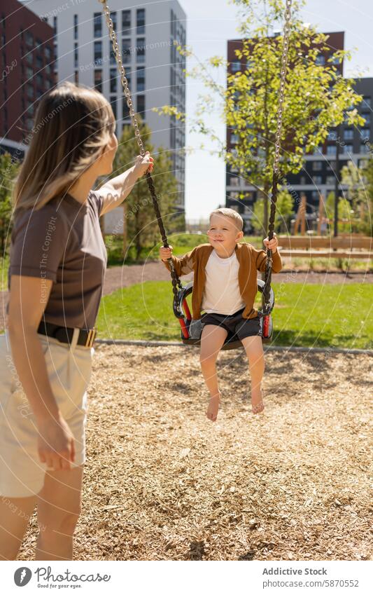 Kleiner Junge genießt die Schaukel, während die Mutter im Park schiebt pendeln Sohn Sommer sonnig Glück Familie im Freien Lächeln Kind Frau schieben Freizeit