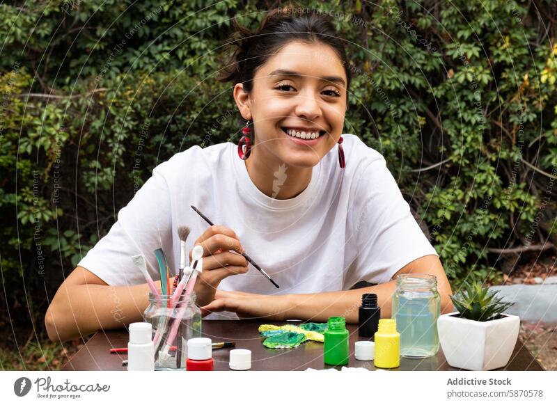 Junge Frau malt mit einem Lächeln im Freien Tonarbeiten Farbe Handwerk Bürste Natur farbenfroh Kunst kreativ Hobby heiter jung Aktivität Basteln künstlerisch