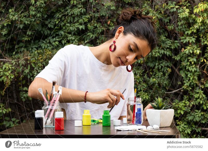 Frau bemalt einen Tontopf im Freien, umgeben von der Natur Farbe Topf Handwerk Kunst Bürste Konzentration Tisch grün üppig (Wuchs) Kreativität Hobby Freizeit