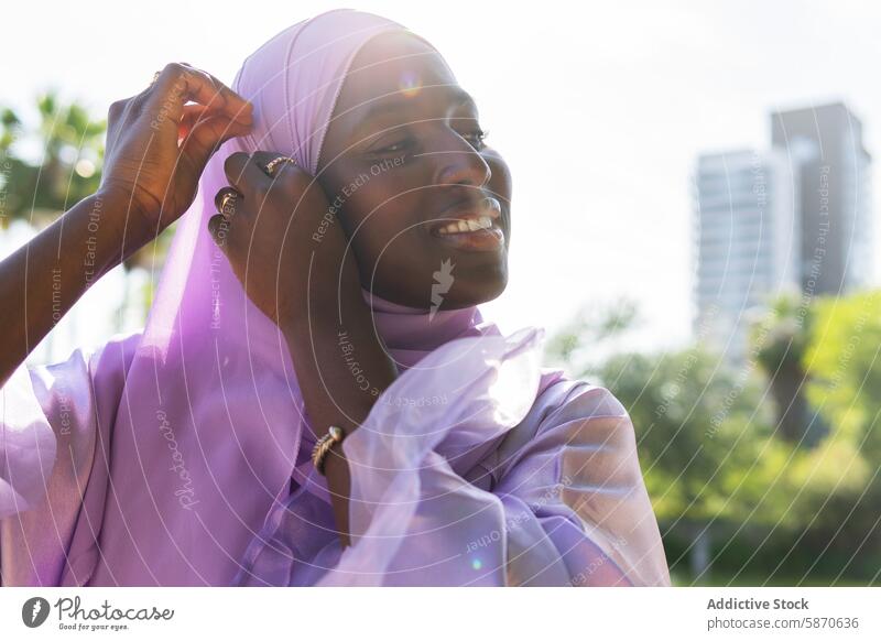 Frau mit lavendelfarbenem Hijab passt ihr Kopftuch im Freien an Park sonnig heiter Wärme Moment Sonnenlicht Liebe Zuneigung fürsorglich Bonden Partnerschaft