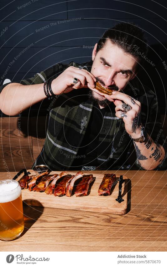 Mann genießt Rippchen mit Bier in einem gemütlichen Restaurant Tattoo Rippe Grillrost Barbecue Essen lässig Stil modern Lebensmittel trinken Mahlzeit speisend