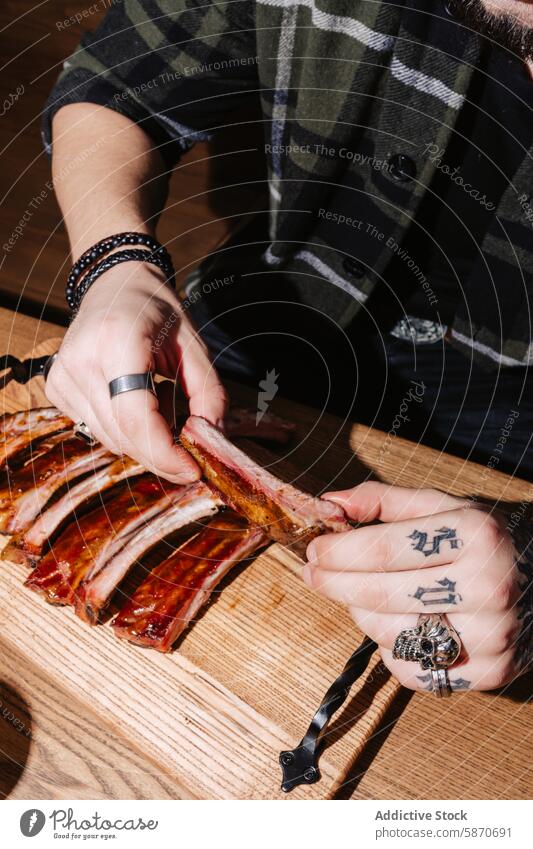 Mann, der an einem Holztisch Rippen auseinander zieht Barbecue Fleisch Tisch Plaid Tattoo Ring Essen zubereiten Lebensmittel ziehend abgesehen Angebot Schneiden