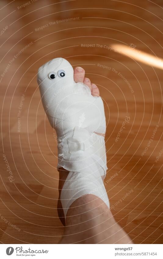 Bandagierter rechter Fuß mit 2 Kulleraugen bandagiert Verband Operation Ruhigstellung Schmerz Gesundheit Wunde Farbfoto Behandlung Heilung Langeweile