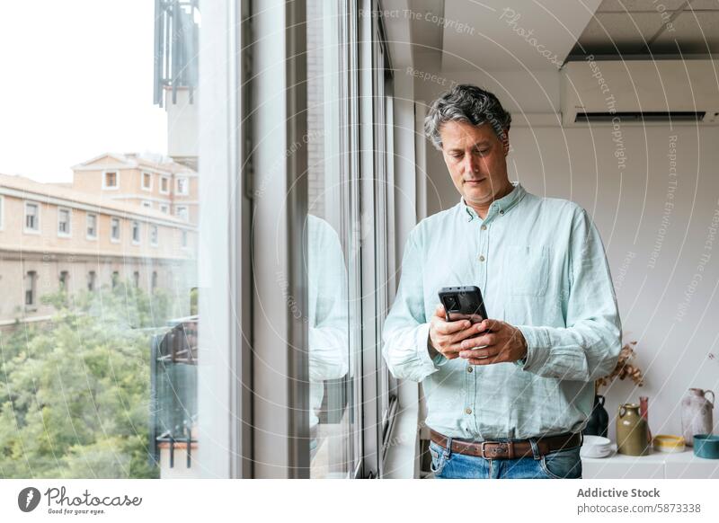 Mann mittleren Alters benutzt Smartphone am Fenster im Büro Technik & Technologie Handy Apparatur Gerät herabsehend urban Architektur modern im Innenbereich