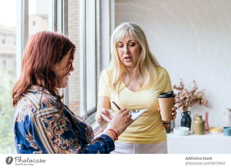 Zwei Frauen besprechen ihre Arbeit mit Kaffee und Smartphone im Büro Coworking Besprechung arbeiten Kaffeetasse Zwischenablage Technik & Technologie Business