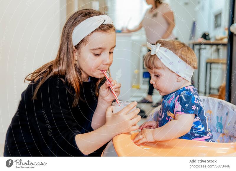 Schwestern teilen sich ein Getränk, während die Mutter im Hintergrund kocht Familie heimwärts Kind Kleinkind Mädchen Essen zubereiten Küche Interaktion