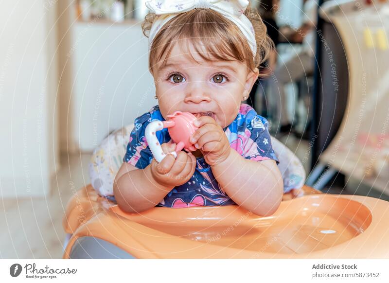 Ein kleines Mädchen genießt ihr Spielzeug zu Hause Baby heimwärts Hochstuhl Kauen spielerisch niedlich Auge Outfit lässig im Innenbereich Szene Kind Kleinkind