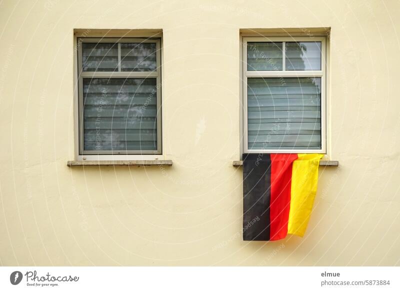 Eine Deutschlandfahne hängt aus einem der beiden Fenster mit geschlossenen Jalousien Fußball Fußballfan schwarz-rot-gold EM WM Europameisterschaft