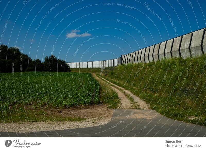 große Mauer auf einer Böschung, an der ein Feldweg entlangführt Grenze Wand Trennung Barriere Weg Grenzweg Schutz Abschottung Landwirtschaft Freiheit