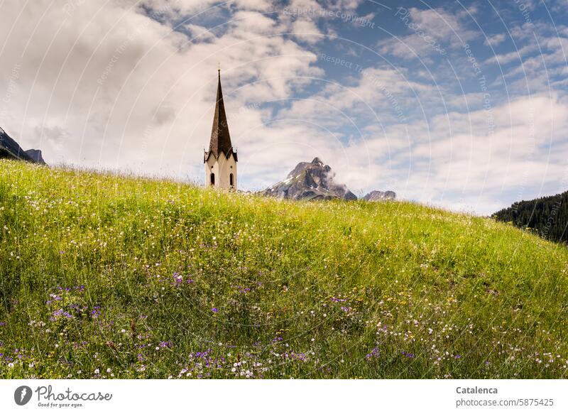 Ein Kirchturm erscheint zusammen mit der Bergspitze hinter dem Grashügel Landschaft Berge Alpen Gipfel Kapelle Spitze Glaube Religion Wiese Wiesenblumen Himmel