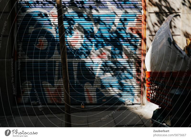 Blätter werfen einen wirren Schatten auf ein Garagentor mit Graffiti bunt ungeordnet chaotisch dynamisch wild blau rot Licht Sonne schräg urban Stadt städtisch