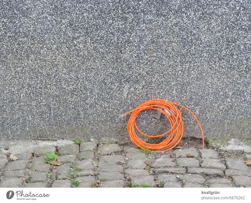 Verkabelt Kabel Technik & Technologie Energie Strom Elektrizität Leitung Hausanschluss Fassade Hauswand Pflastersteine grau orange aufgerollt Verbindung