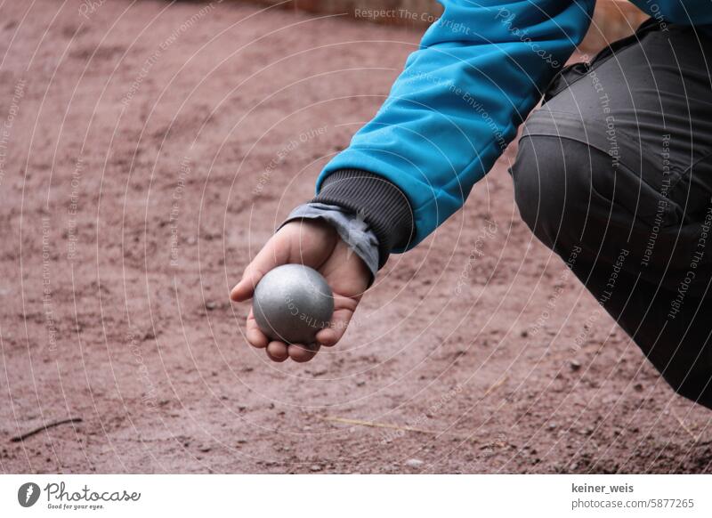 Boulekugel in der Hand eines Boulespielers beim Pétanque oder Boule auf roter Erde Petanque Kugel Spielen Bouelspiel Petanqueplatz Bouleplatz Metallkugeln