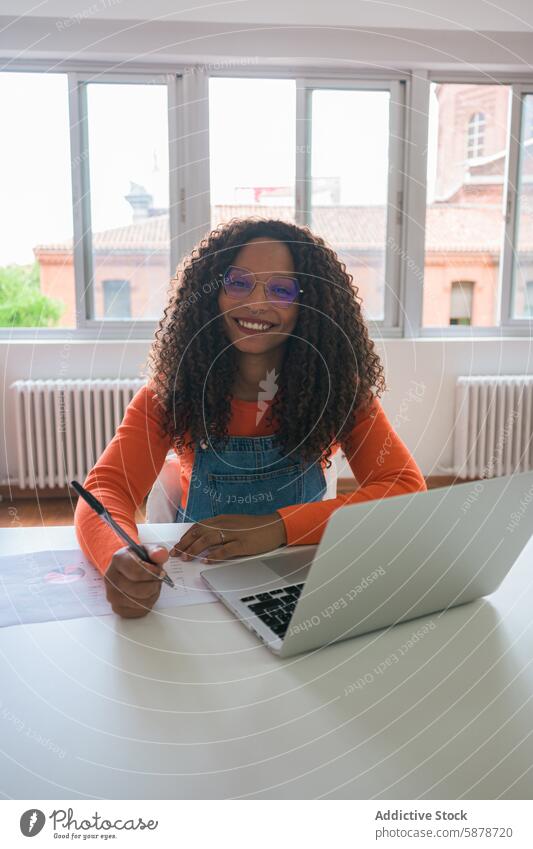 Lächelnde junge Frau bei der Arbeit in einem hellen Büro Laptop Schreibtisch Business professionell Brille krause Haare heiter modern Technik & Technologie