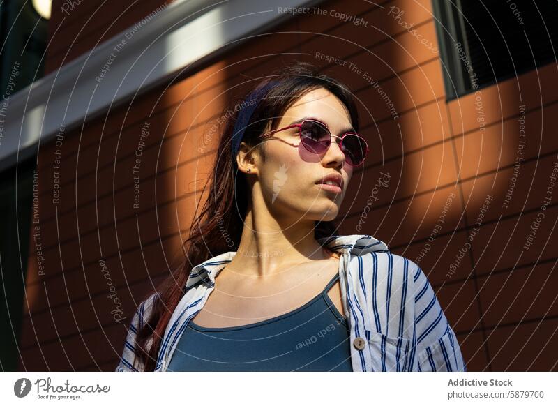 Lässige Frau mit Sonnenbrille, die sich an eine Backsteinmauer lehnt Frühling Sonnenlicht urban lässig Stil Mode jung trendy Wand Baustein im Freien Großstadt