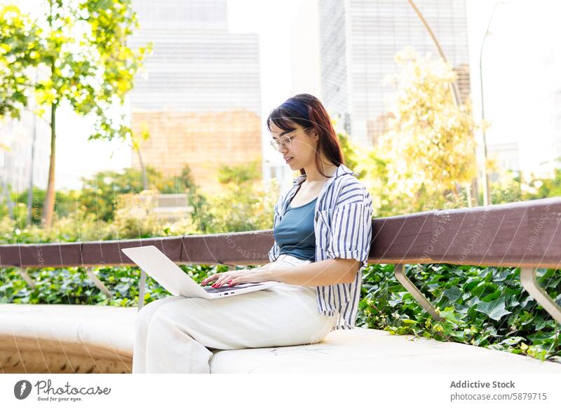 Junge Frau arbeitet im Freien mit Laptop in einem Stadtpark Park urban sitzend Bank arbeiten jung professionell Technik & Technologie Grün Gebäude Großstadt