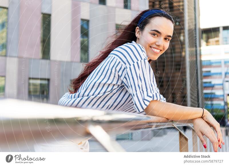 Junge Frau in gestreifter Bluse lächelnd in städtischer Umgebung Frühling Porträt urban Lächeln heiter Reling Gebäude sonnig Tag jung rote Haare blau Umwelt