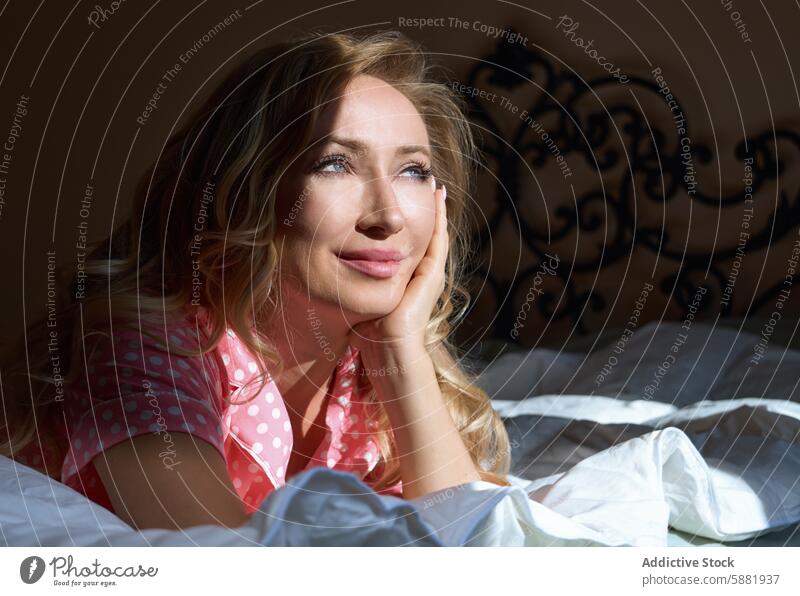 Verträumte blonde Frau, die sich im Bett entspannt, beleuchtet vom Sonnenlicht entspannend Morgen friedlich Gelassenheit beschaulich Starrer Blick Ausdruck