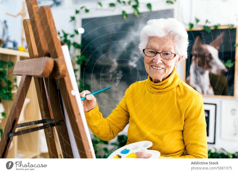 Ältere Frau malt auf Leinwand in einem hellen Atelier älter Senior reif Malerei Kunst heiter kreativ Hobby Anstreicher Bürste Palette künstlerisch gelb