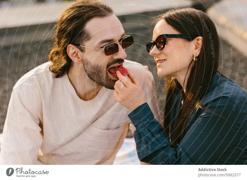 Romantischer Moment mit einem Paar, das sich auf einer Dachterrasse eine Erdbeere teilt Erdbeeren Freude Sonnenbrille lässig spielerisch Mann Frau Teilen sonnig